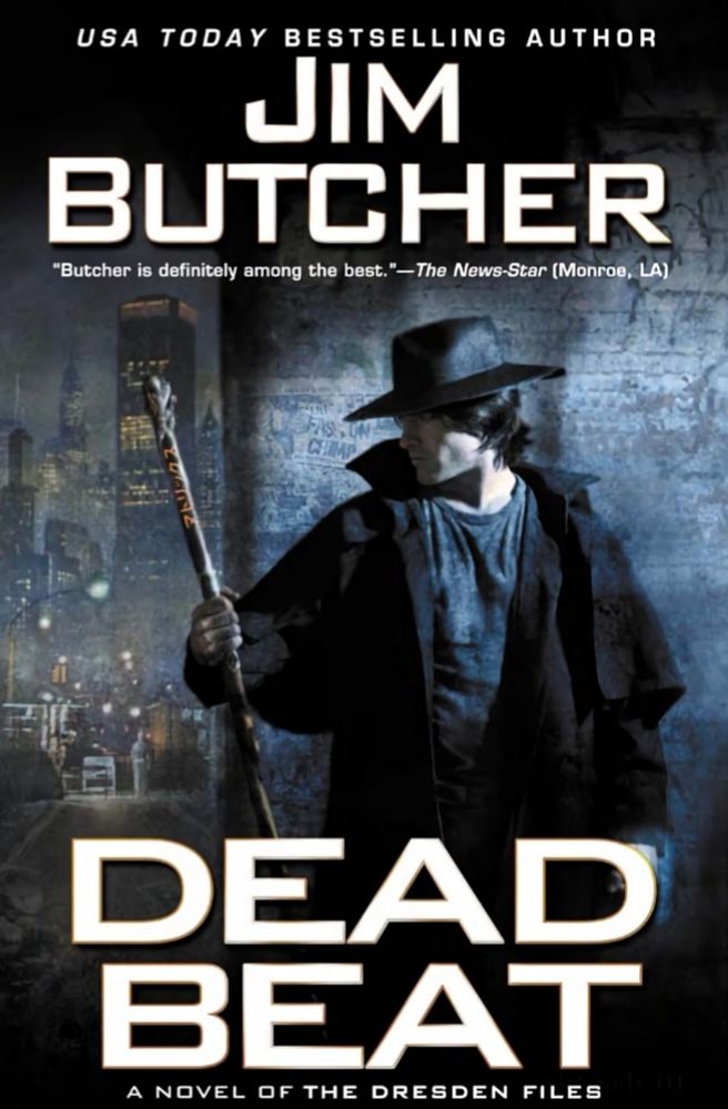 The front cover for Dead Beat by Jim Butcher showing the side profile of a man in a black trenchcoat wearing a black hat and holding a staff. In the background is a skyline of a major city with skyscrapers and a street. It is nighttime and slightly foggy. 
