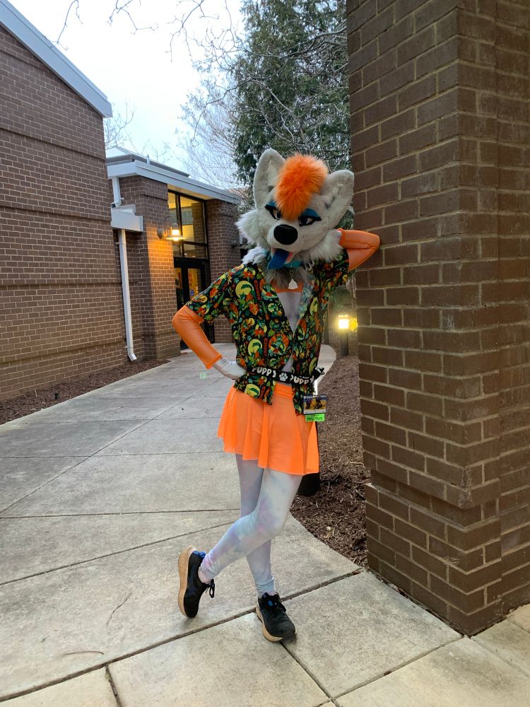 Surge wearing an orange skirt, orange crop top under a hawaiian-style shirt leaning against a pillar