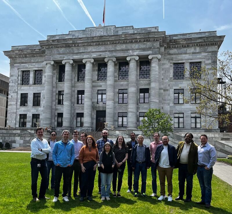 Photo of workshop attendees standing on the Harvard Quad green in front of Gordon Hall, large stone columned building 