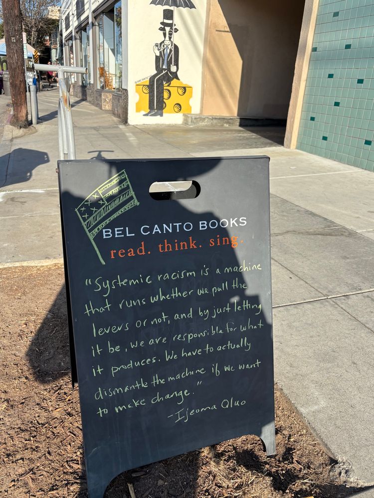 Black chalkboard sign at Bel Canto Books that reads "Systemic racism is a machine that runs whether we pull the levers or not, and by just letting it be, we are responsible for what it produces. We have to actually dismantle the machine if we want to make change.”
- Ijeuma Oluo