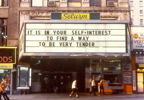 A photograph of a theater marquee (maybe in Times Square) with the message "IT IS IN YOUR SELF-INTEREST TO FIND A WAY TO BE VERY TENDER"