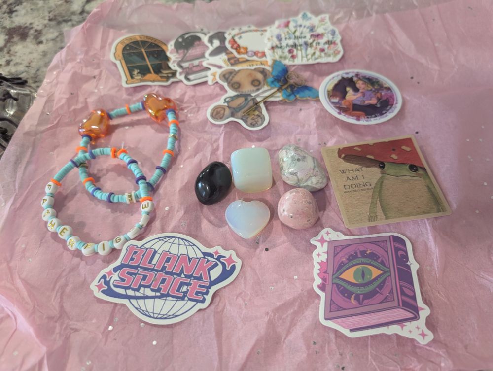 A collection of stickers, friendship bracelets, and crystals laid out on pink sparkly tissue paper.