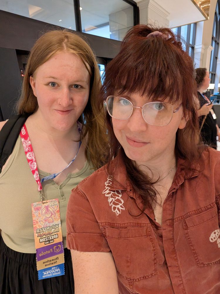 A selfie of me and Bree! Bree on the left is wearing a soft green shirt and her GDQ badge. I on the right have my hair up in a high pony and am wearing a red collared shirt. I have no badge on because I'm evil like that.