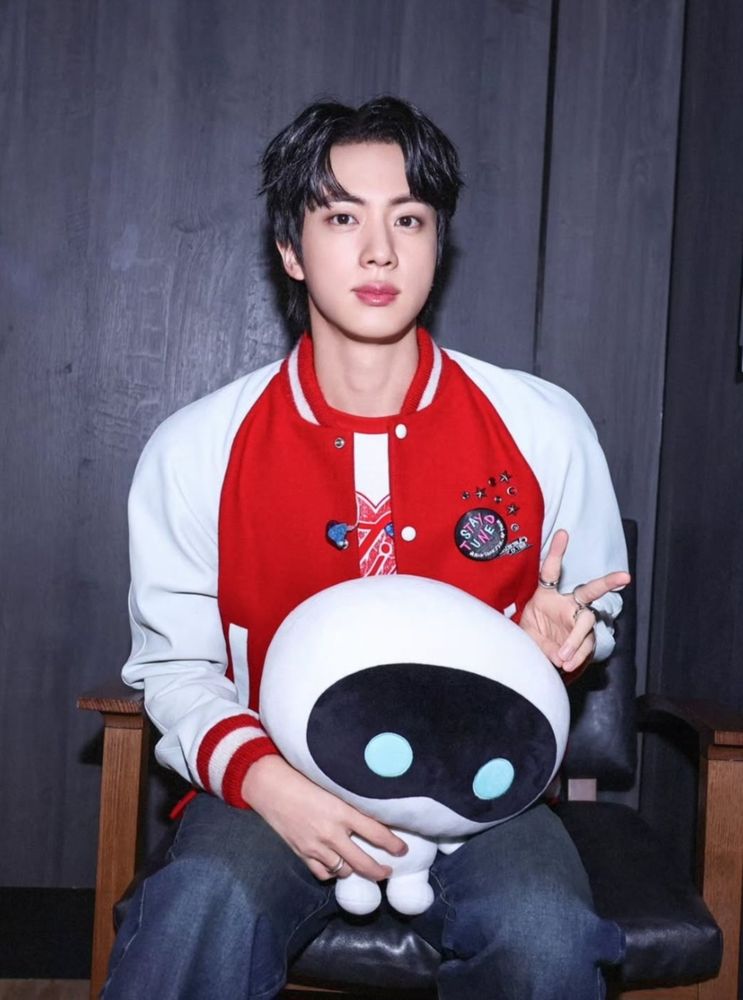 jin looking really hot in a red letterman style jacket, forehead out doing a peace sign. the prodigal child wootteo sits in his lap