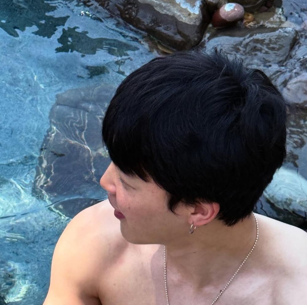 a very cute naked looking jimin in a pool. shown bare shoulders up with his thick hair starting to grow back into its classic three layers, and a few freckles on his cheek
