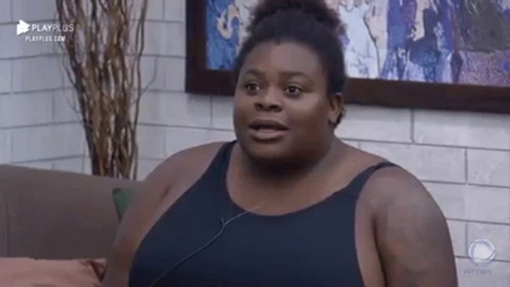 a very fat woman is sitting on a couch wearing a black tank top and headphones .