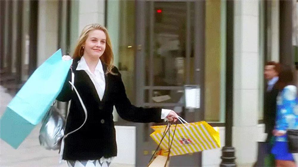 a woman in a black jacket is carrying shopping bags in front of a building