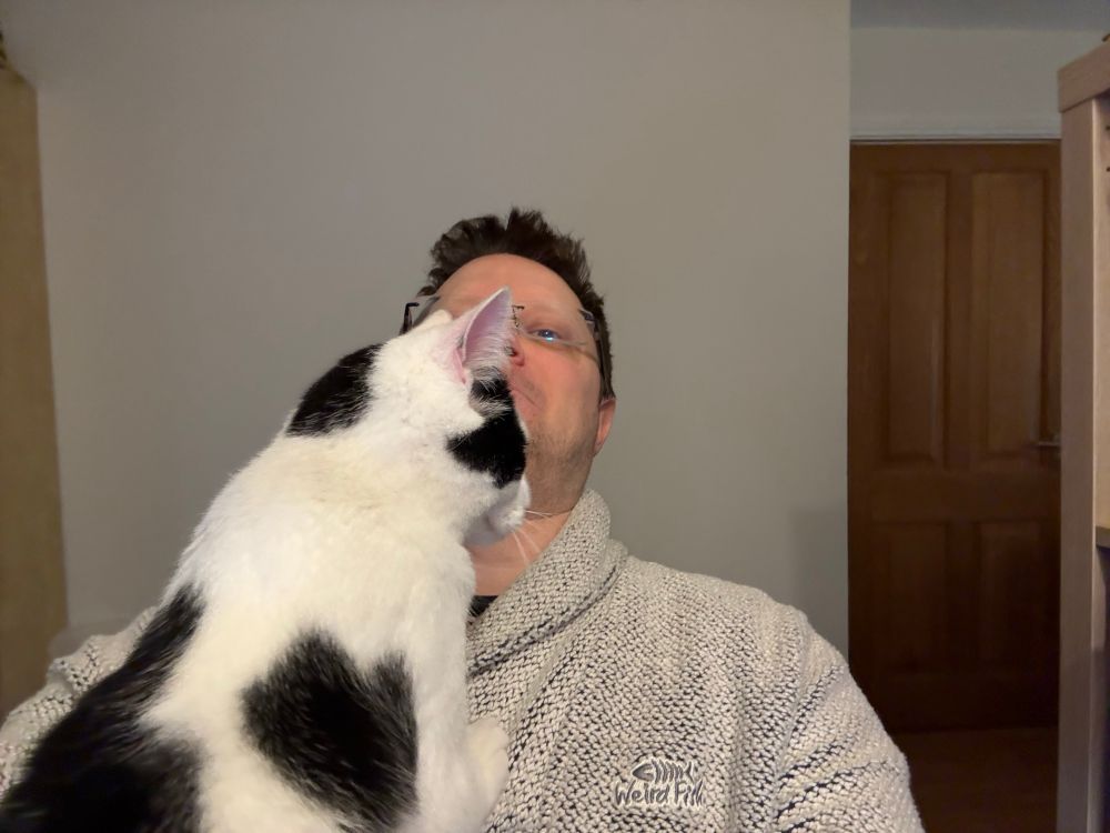 Selfie of the author. there is a white and black cat, Xander, trying to crawl up into his face .