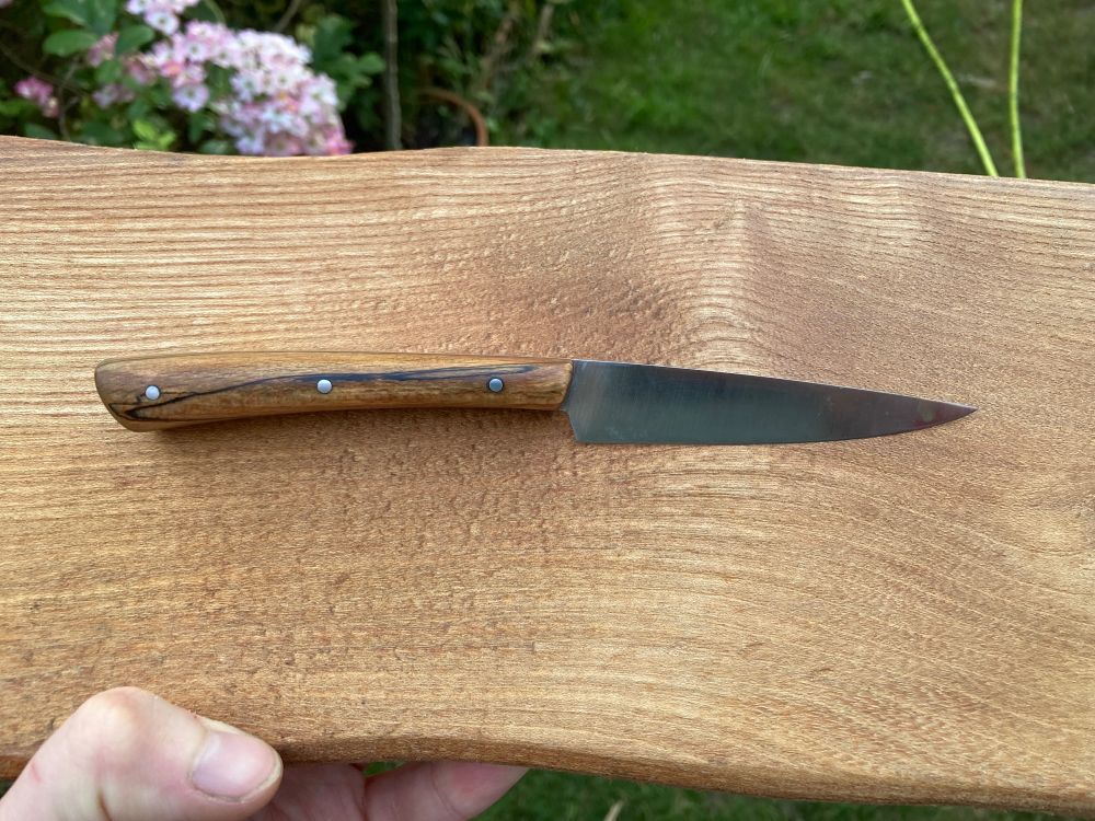 Small steak knife, handled in spalted beech with stainless steel pins. It is resting on a wooden board.