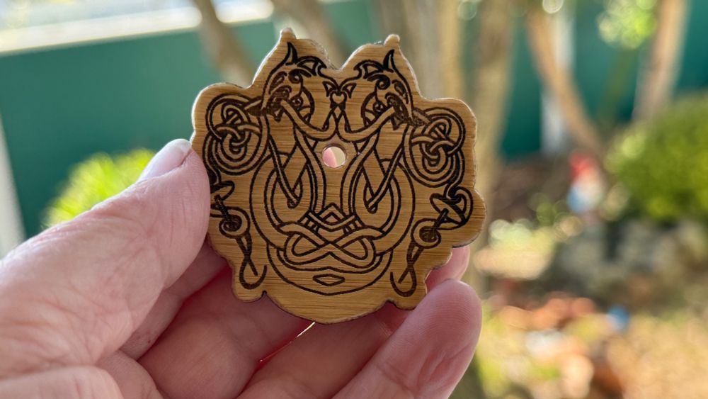 A diz for making combed top from hand comb, hackle or deum carder. The diz is made of wood with a Celtic dragon design laser engraved into it.