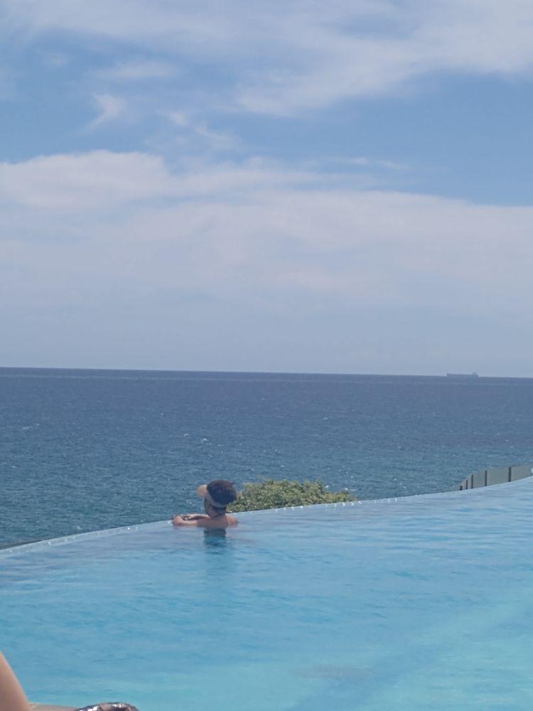 Piscina de borda infinita virada para o mar. Mulher de viseira bege e cabelo afro olhando o horizonte 