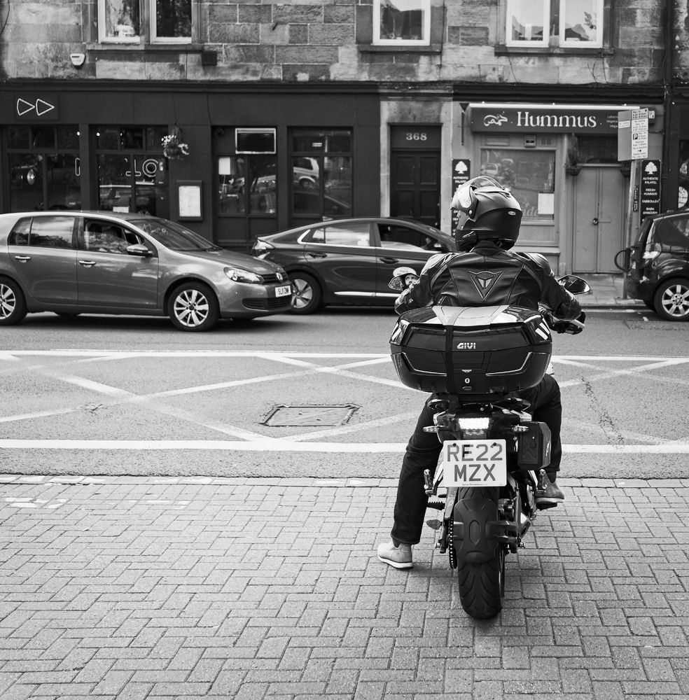 A biker pauses at a junction. His face visible in the side mirror.