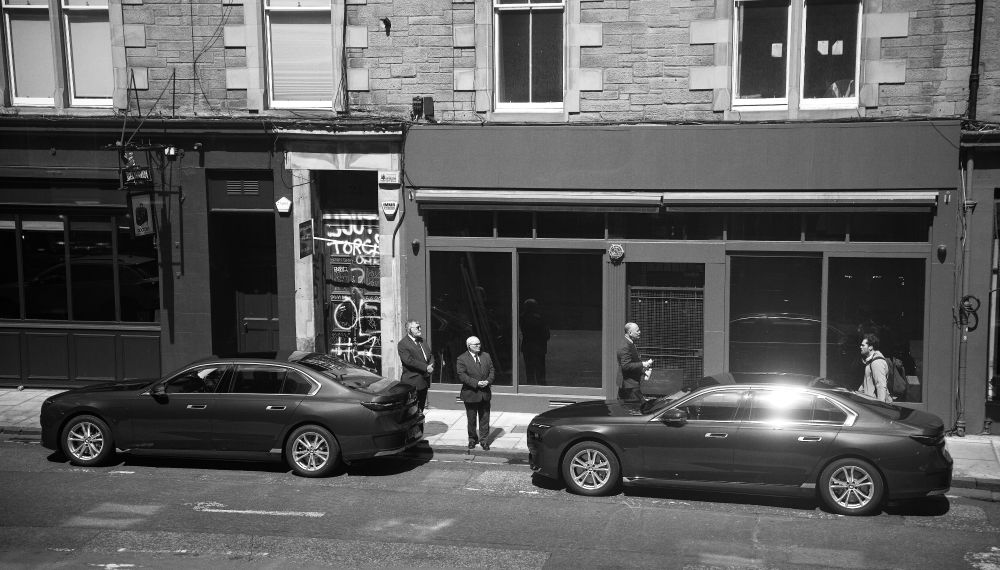 Two secret servicey-looking (they wish!) men stand guard over expensive cars waiting and watching for... I dunno, someone important probably? Or someone rich.