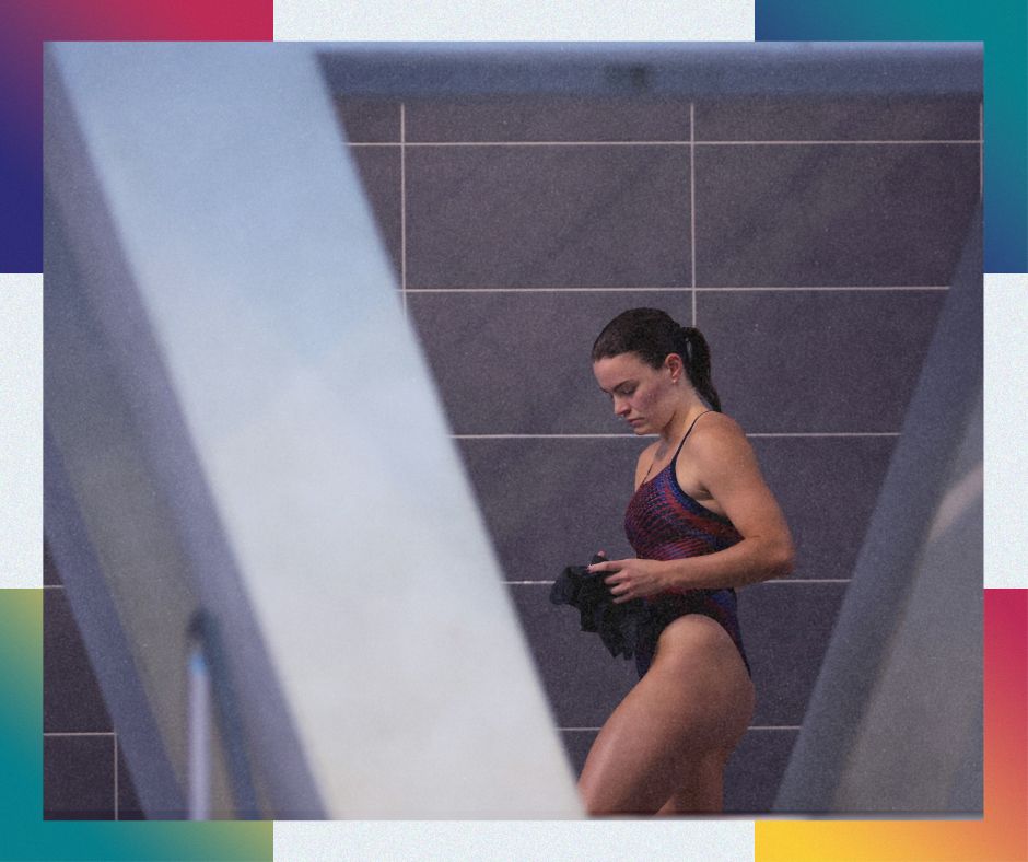 A photo of Amy Rollinson in a purple, pink and black swimsuit. She has her dark hair tied up in a ponytail and is looking downwards.