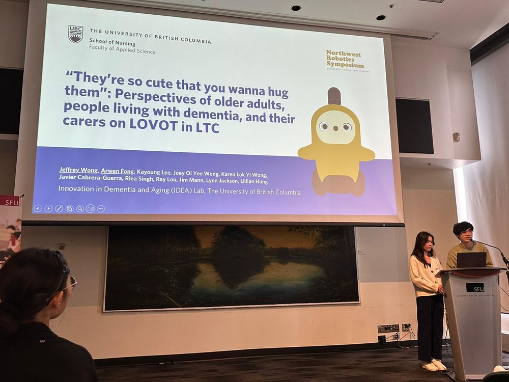 Jeffrey Wong and Arwen Fong present at the Northwest Robotics Symposium, with a large slide behind them titled: “They’re so cute that you wanna hug them”: Perspectives of older adults, people living with dementia, and their carers on LOVOT in LTC.