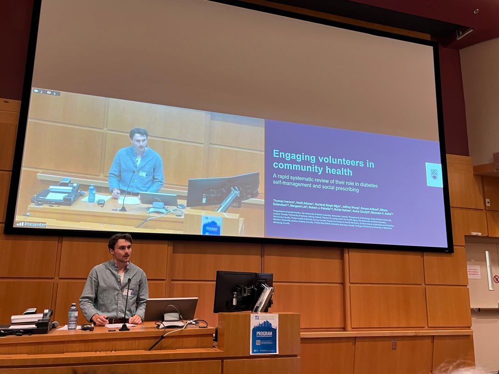 Thomas Iverson stands at a podium delivering an oral presentation titled “Engaging Volunteers in Community Health” at the 2025 INCREASE BC conference. A large screen behind him displays the title slide of the rapid systematic review.