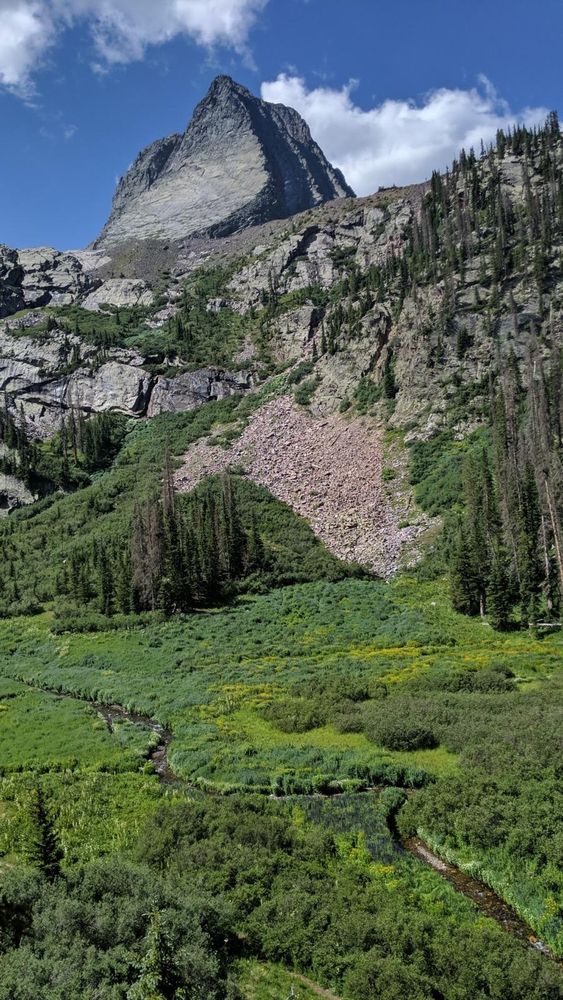 A vertical landscape shot of a place called Vestal Bason depicting a meandering creek in the foreground and a massive, tooth-shaped peak in the background.