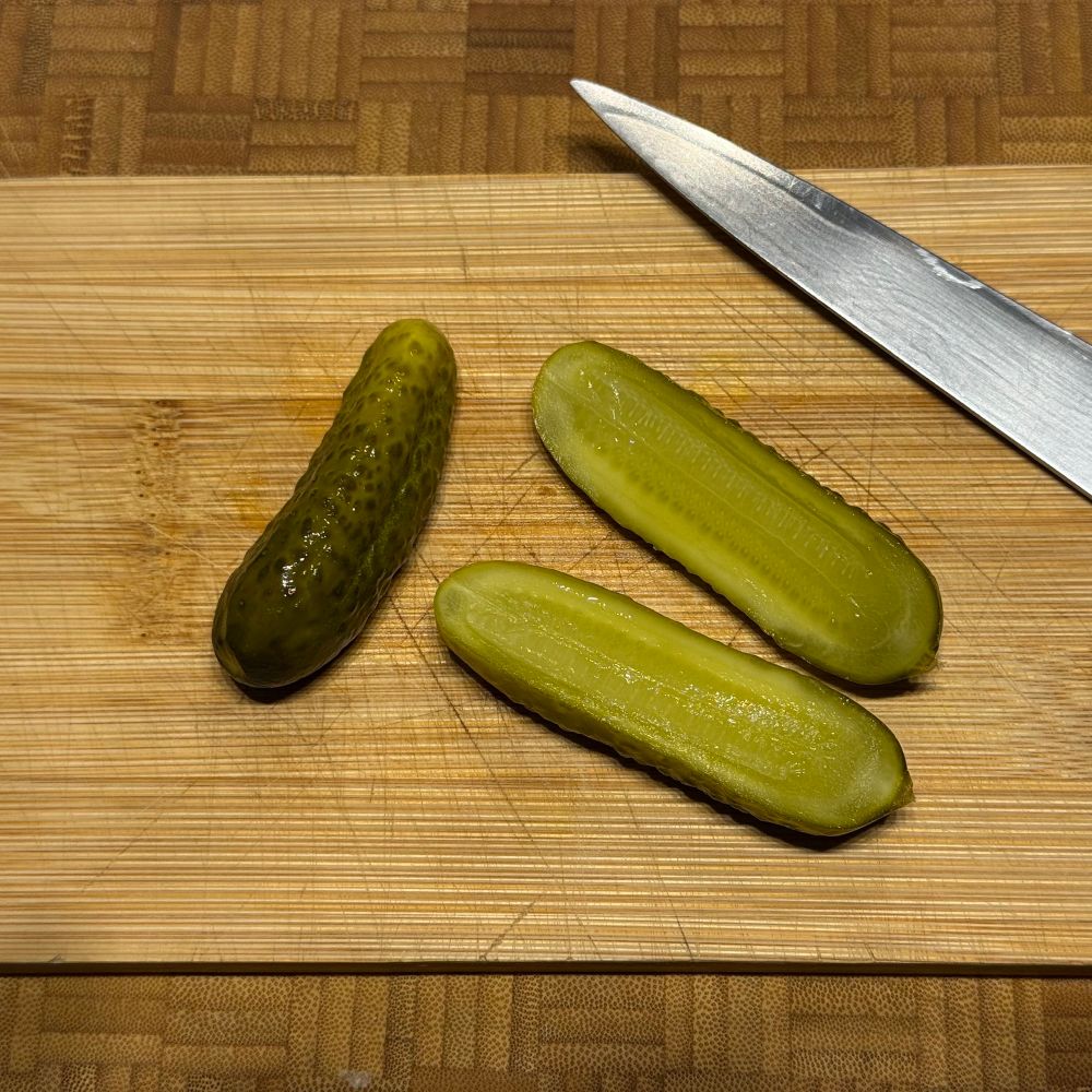 Aufgeschnittene Gewürzgurken auf Schneidbrett mi Messer.