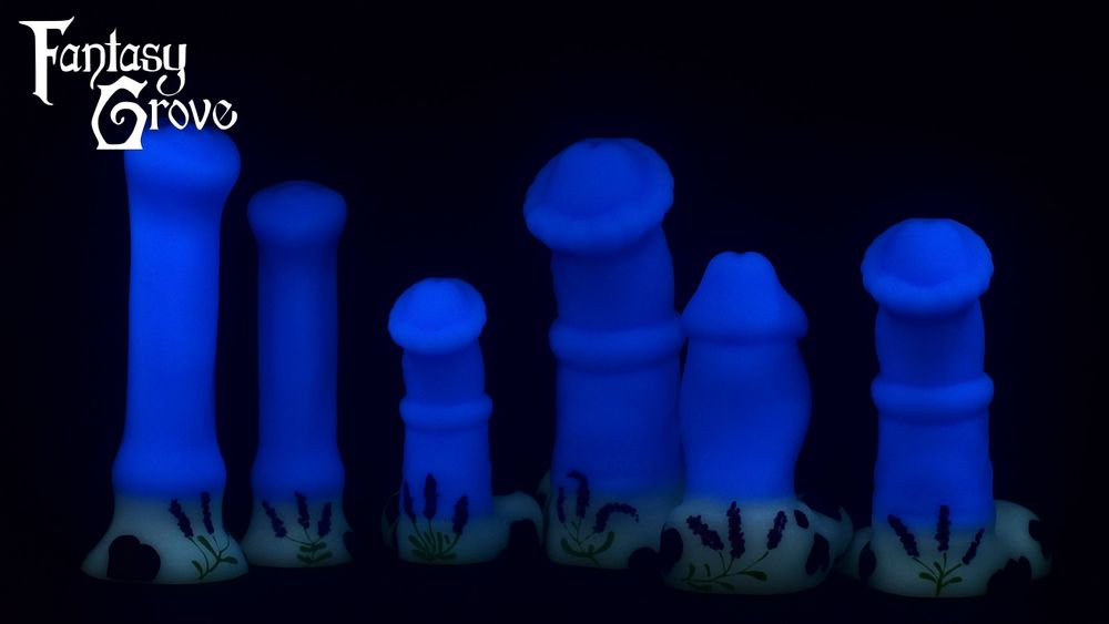 A lineup of dildos in the dark displaying blue glow in the dark shafts, and white glow in the dark bases with the outline of dark purple cow spots and hand painted lavender flowers. From left to right there's a medium and large simplified equine model, a small and large chunky equine model, a stout humanoid model, and a medium chunky equine model.