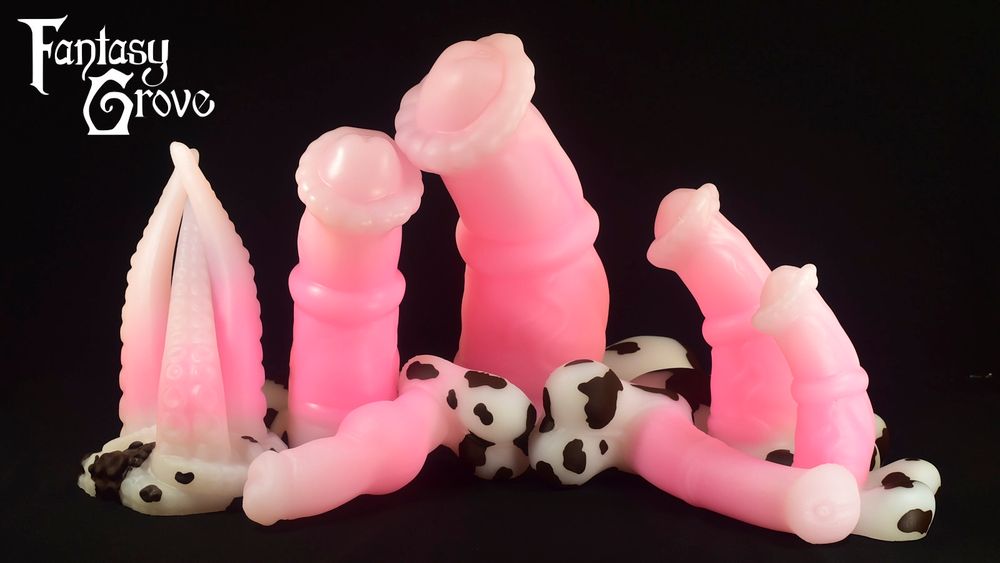 A lineup of dildos with a light to medium pink fade on the shaft and white bases with brown spots. From left to right there's a three shafted tentacle model, a large chunky equine, a XXL chunky equine, and a medium and small chunky equine. In the front is a canine model and a longer thinner equine model.