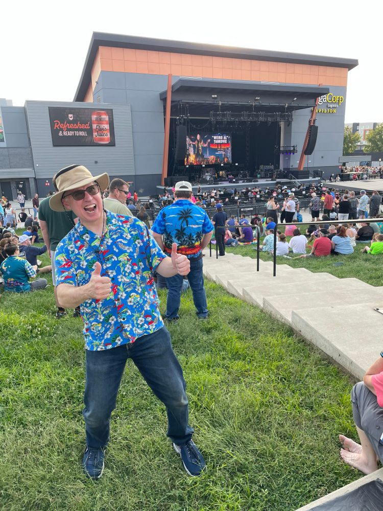 A goofball guy in a Smurf shirt giving two thumbs up at a Weird Al concert.