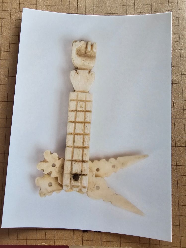 A tiny manicure set carved from bone by someone living in prison. It looks like an arm with a grid patterned sleeve and a solidarity clenched power fist 
