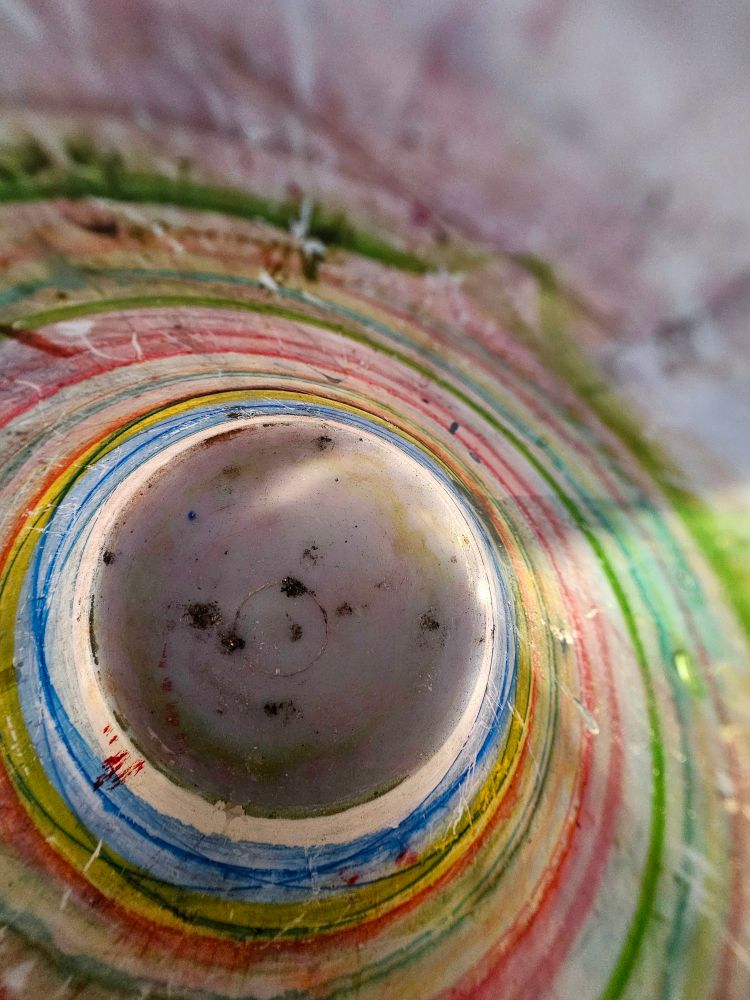 Multi coloured paint pigment lines gathered around the inside of a plastic mug 