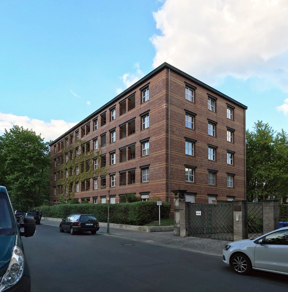 Vista de un bloque de viviendas con fachada de ladrillo en dos colores. El bloque es prismático desde esta vista, tiene cuatro plantas de altura y un sistema de ventanas cuadradas y balcones pareados muy pautado y regular
