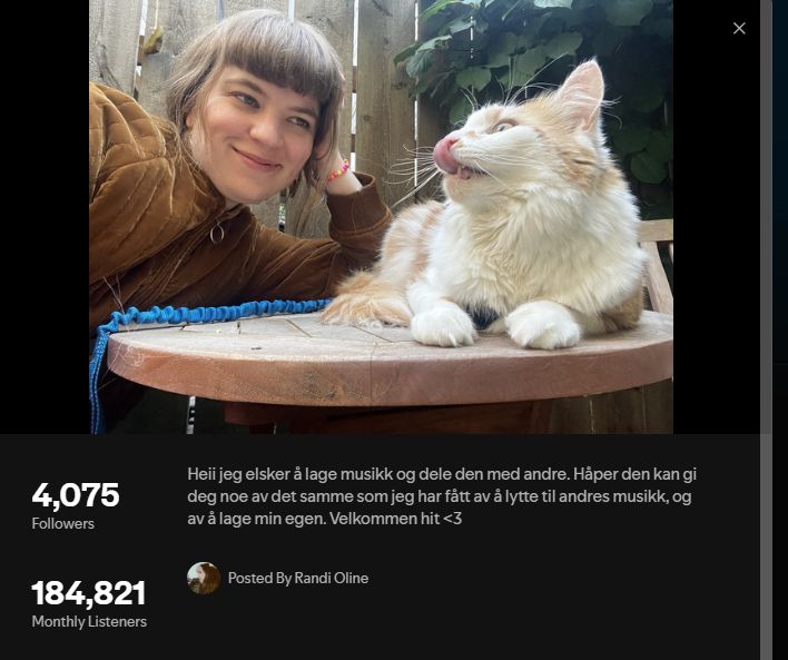 Randi Oline, a Norwegian singer, smiling at a white and orange cat that is licking its nose.