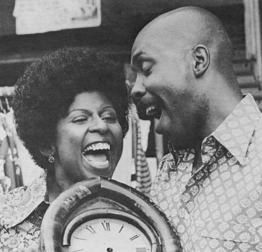 Black and white headshot of Susan and Gordon from Sesame Street holding a clock 