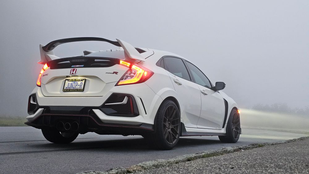 a Championship White FK8 Civic Type R, as viewed from behind, with headlights casting beams through thick fog on the far side of the vehicle. 