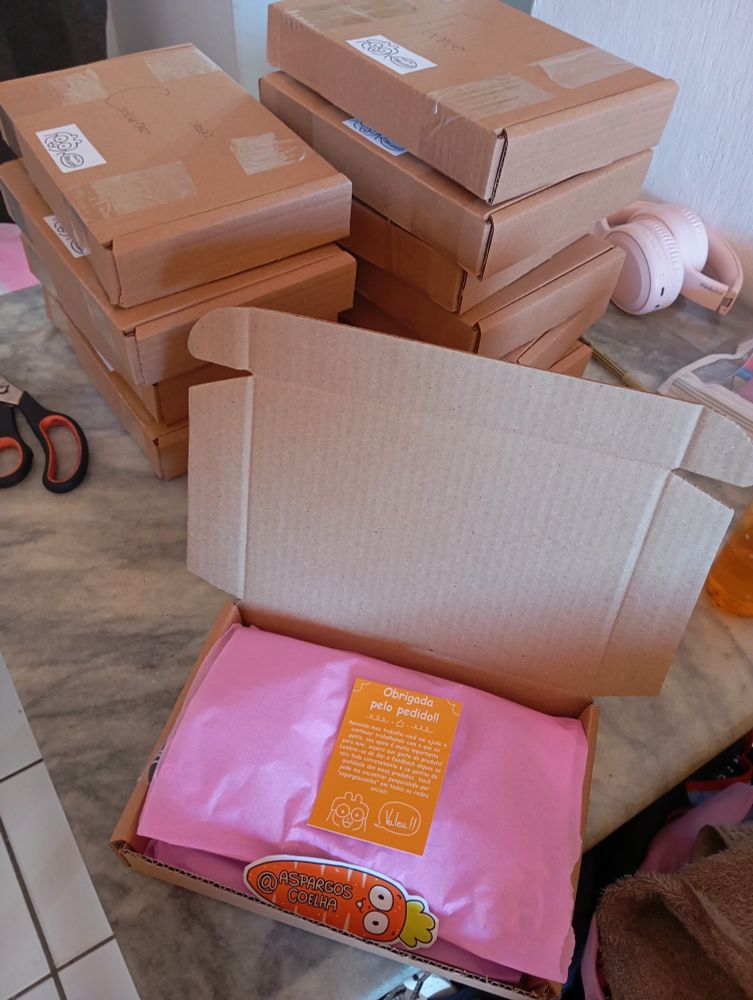 caixas de papelão em pilha e uma aberta na frente com um recado de agradecimento, papel rosa e meu cartão de visitas