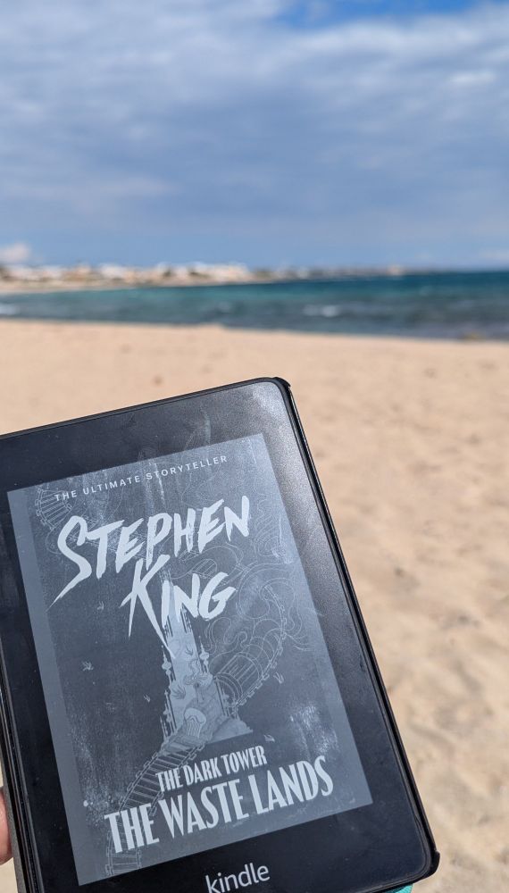 Photo of kindle displaying cover of The Waste Land by Stephen King with beach and sea in the background 