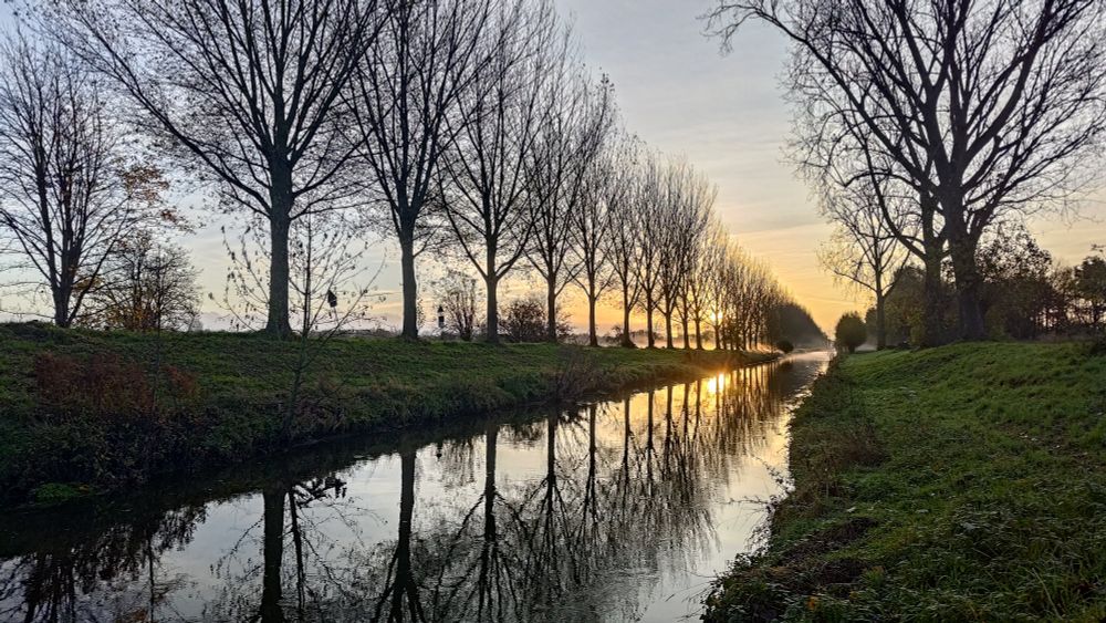 Ein Blick längs der Niers, im Hintergrund geht die Sonne auf, kahle Bäume rechts und links