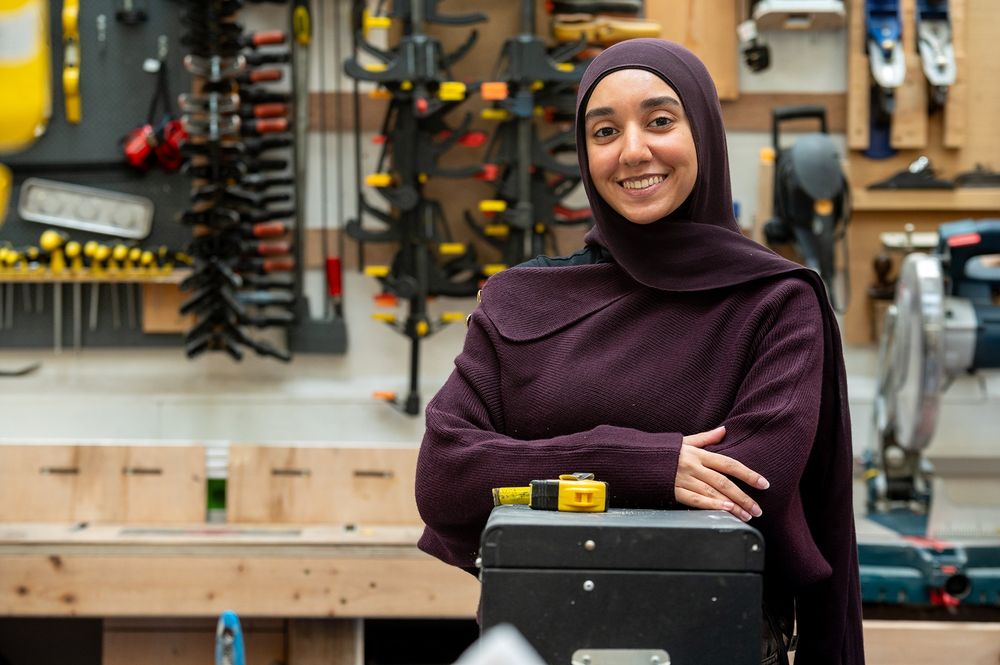 Fareda stands with her arms folded, smiling in a workshop
