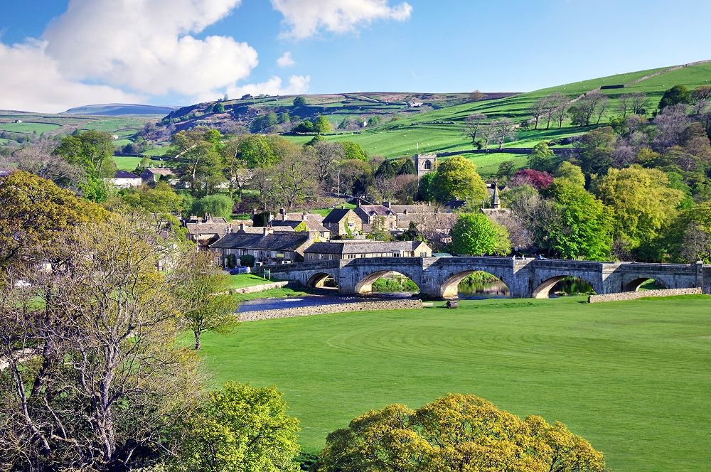 Burnsall village green with a picturesque river and bridge behind