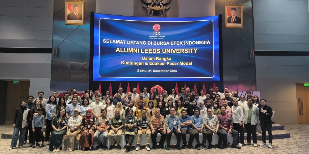 A group photo in front of a large banner at an event. The banner reads "Alumni Leeds University"