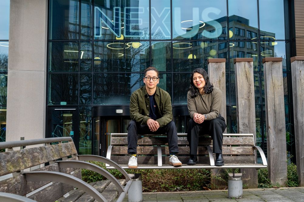 Two individuals sit on a bench outside the NEXUS building at the University of Leeds