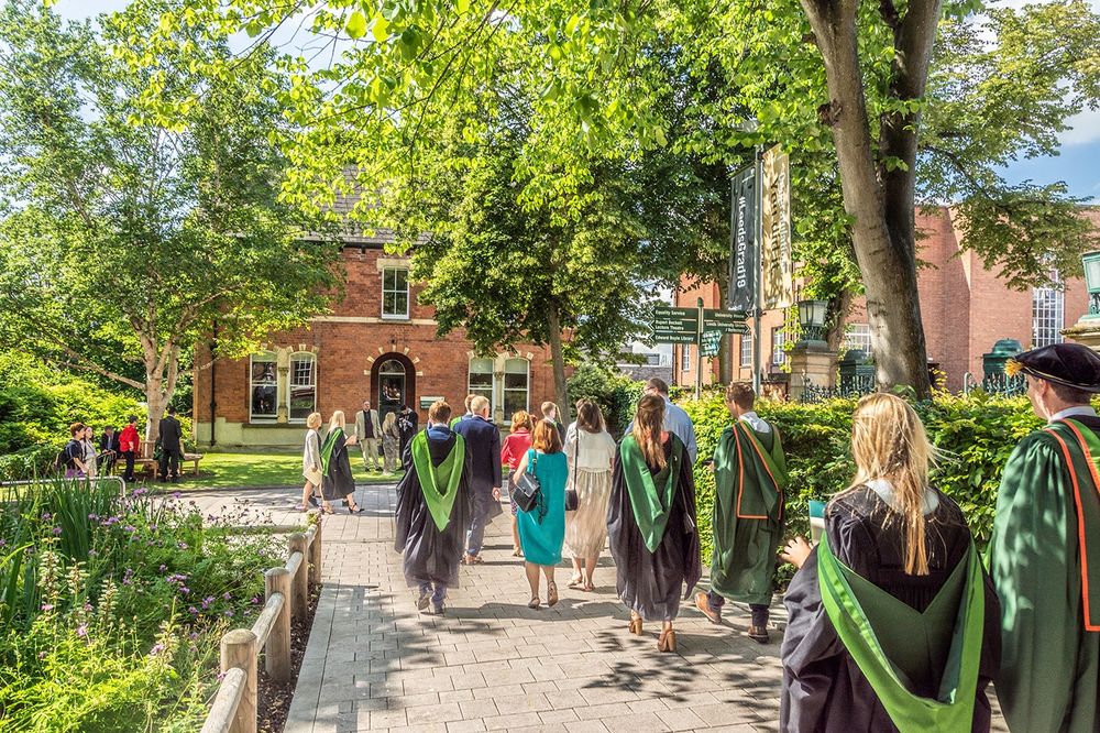 Graduates in gowns walk towards a red brick building on the University of Leeds campus