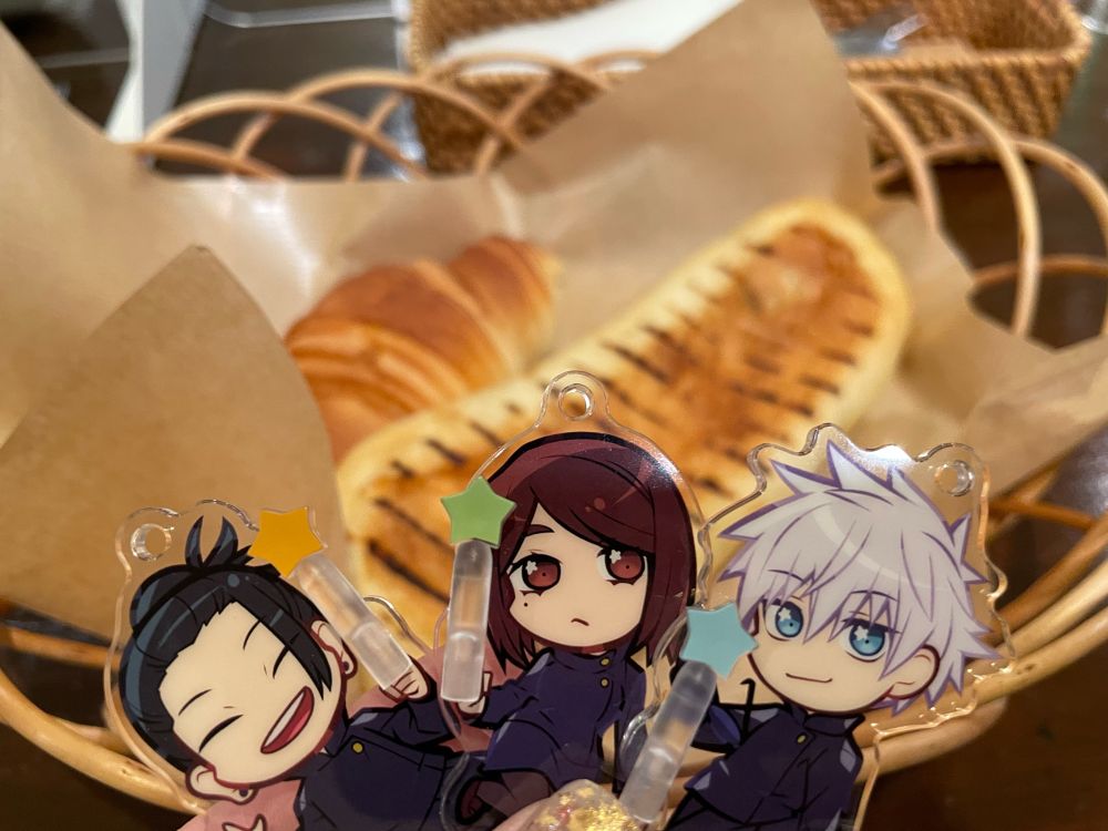 パンふたつとアクリルキーホルダーが写った写真。クロワッサンと焼き目のついたパニーニ、パニーニは生ハムだったと思う。手前に呪術廻戦、夏油・家入，五条のキーホルダー。