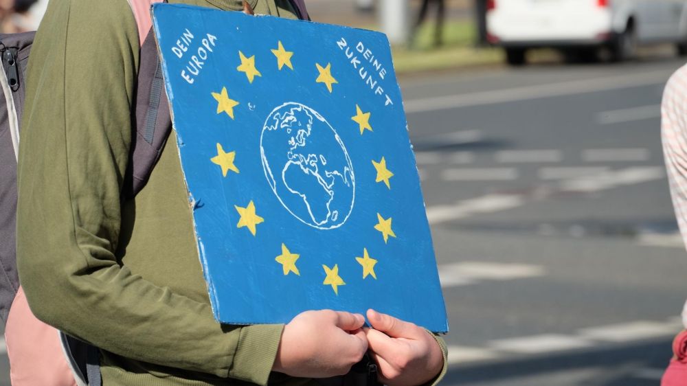Eine Person trägt ein schild mit der eu-fahne und einer Erde zwischen den gelben Sternen. Dein Europa, deine Zukunft