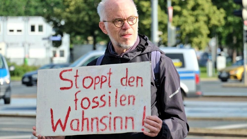 Ein Mann hält ein Schild. Stoppt den fossilen Wahnsinn.