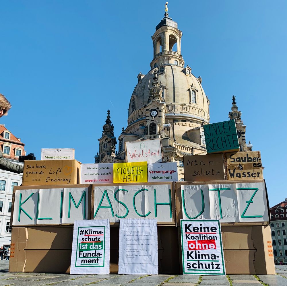 Pappkartons mit politischen Wünschen stehen vor der Frauenkirche. Sie richten sich an die Bundesregierung: keine Koalition ohne Klimaschutz; Das Fundament ist Klimaschutz. Kinderrechte, Wohlstand, Sicherheit, Artenschutz und mehr.