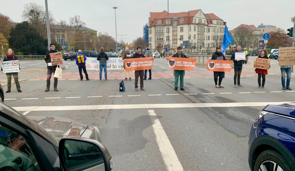 Menschen blockieren den Fritz-Foerster-Platz in Dresden. Sie halten Banner wie „Physik verhandelt nicht“