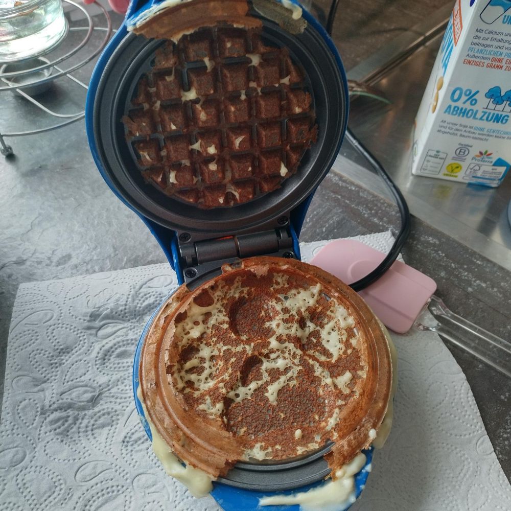 ein gfeöffnetes kleines Waffeleisen mit Pfotenabrdruck-Motiv mit Teigresten. Die Teigreste kleben nur an den Heizplatten und am Rand. Im innern der Teigwaffel ist nichts. Die Waffel besteht nur aus Rand, der an Heizplatten klebt.