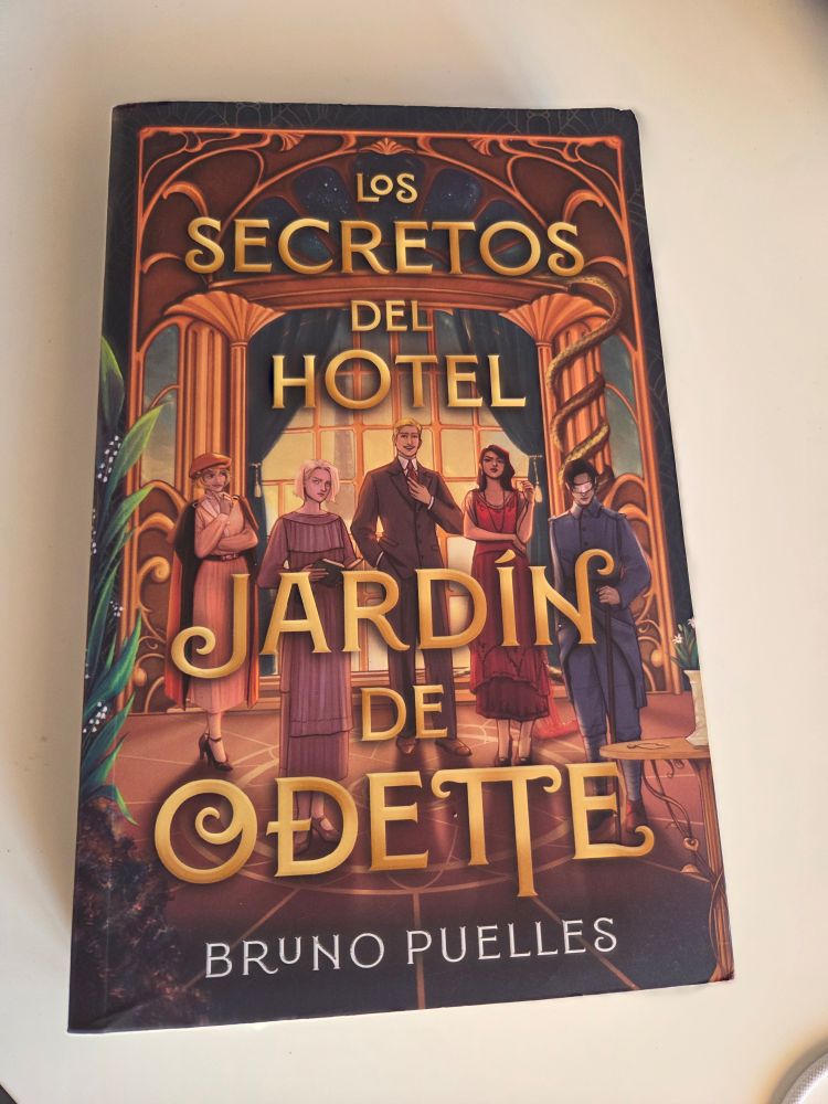 Cover for Bruno Puelles' Los Secretos del Hotel Jardìn de Odette. It shows 5 people, each very different from one another, standing in a hotel lobby that's richly decorated and built.