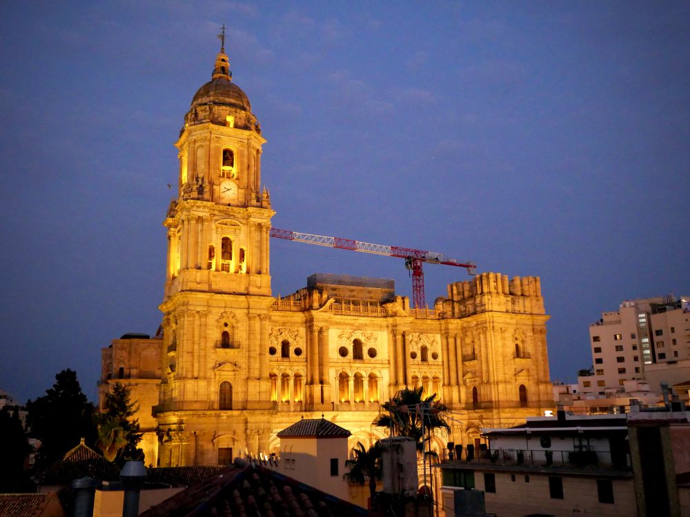 A photo of Santa Iglesia Catedral Basílica de la Encarnación de Málaga at dusk. It is lit up and looks like gold. 