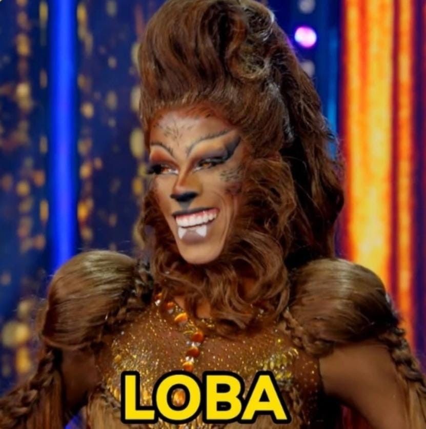 Imagem da drag queen brasileira Melody Queen no programa Drag Race Brasil. A diva está com um look feito de cabelos e toda montada e maquiada em referência ao lobisomem, que faz parte do folclore brasileiro. Na imagem há o texto "Loba