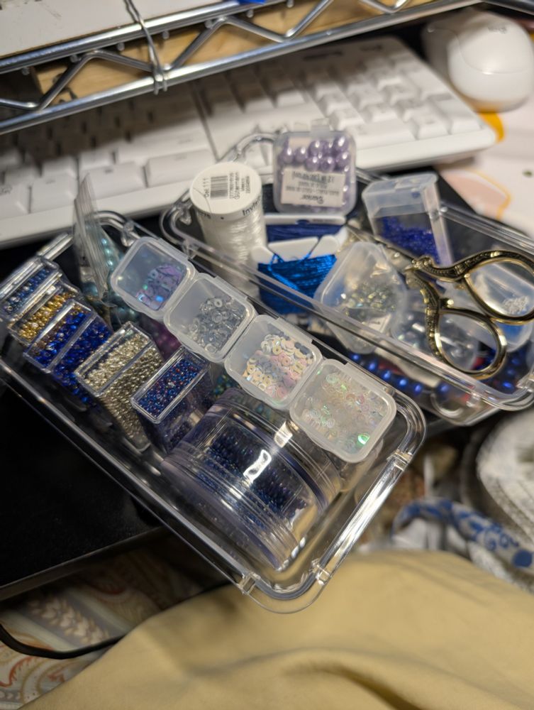 Photo of two small containers full of even smaller tiny containers holding a variety of seed beads, pearls, sequins, embroidery floss, and clear beading thread.