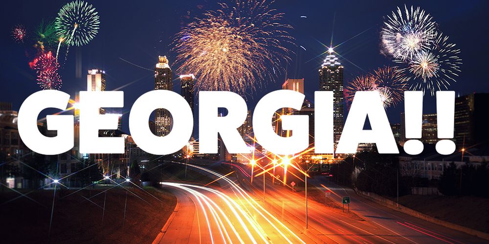 Fireworks at night over downtown Atlanta with foreground of highway with long exposure headlights creating a light path. Over the image in large white capital letters is "GEORGIA!!"